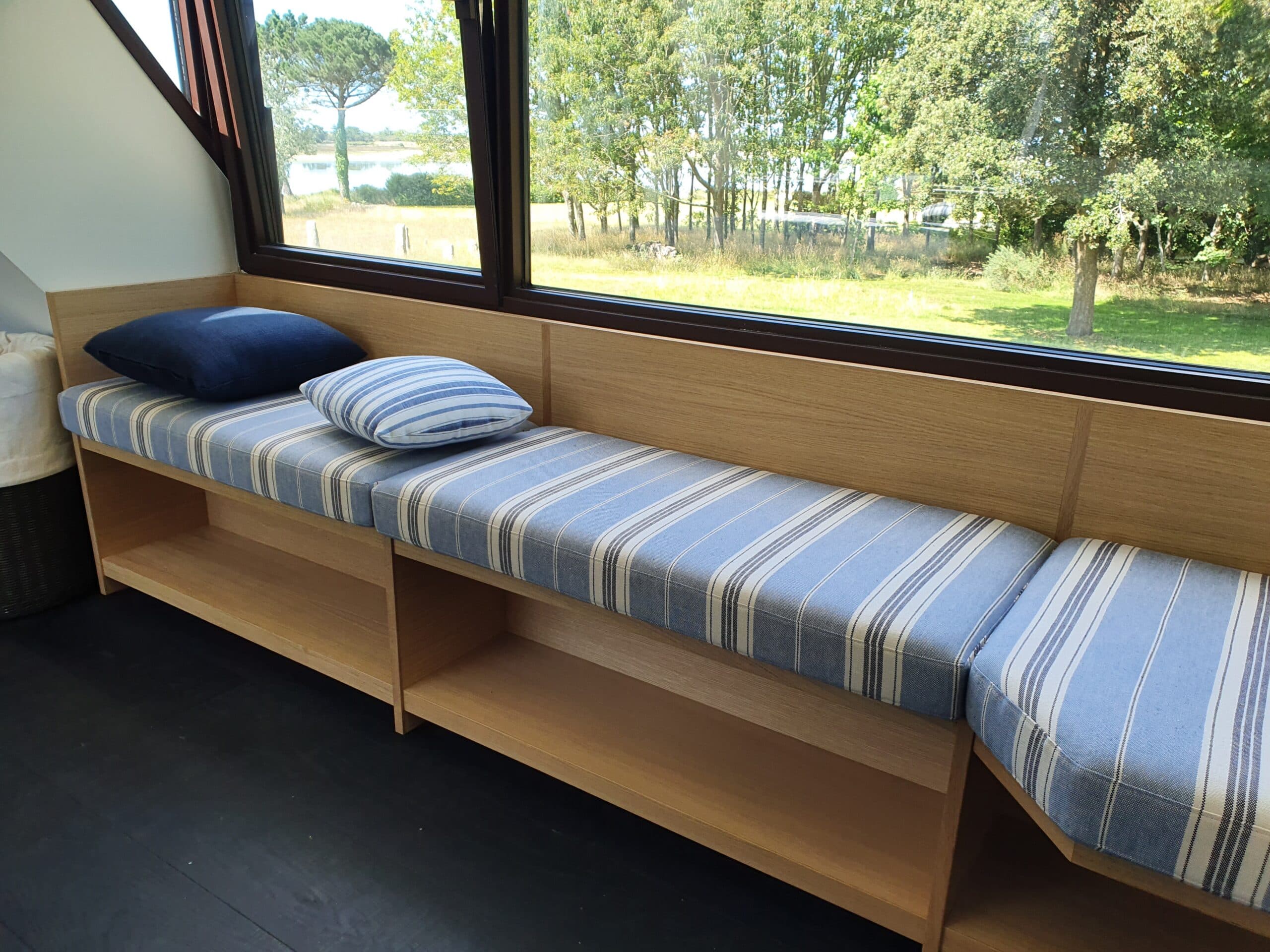 Banquette en bois à coussins rayés devant une baie vitrée