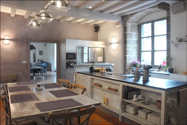 Cuisine de caractère avec îlot gris, table et poutres apparentes