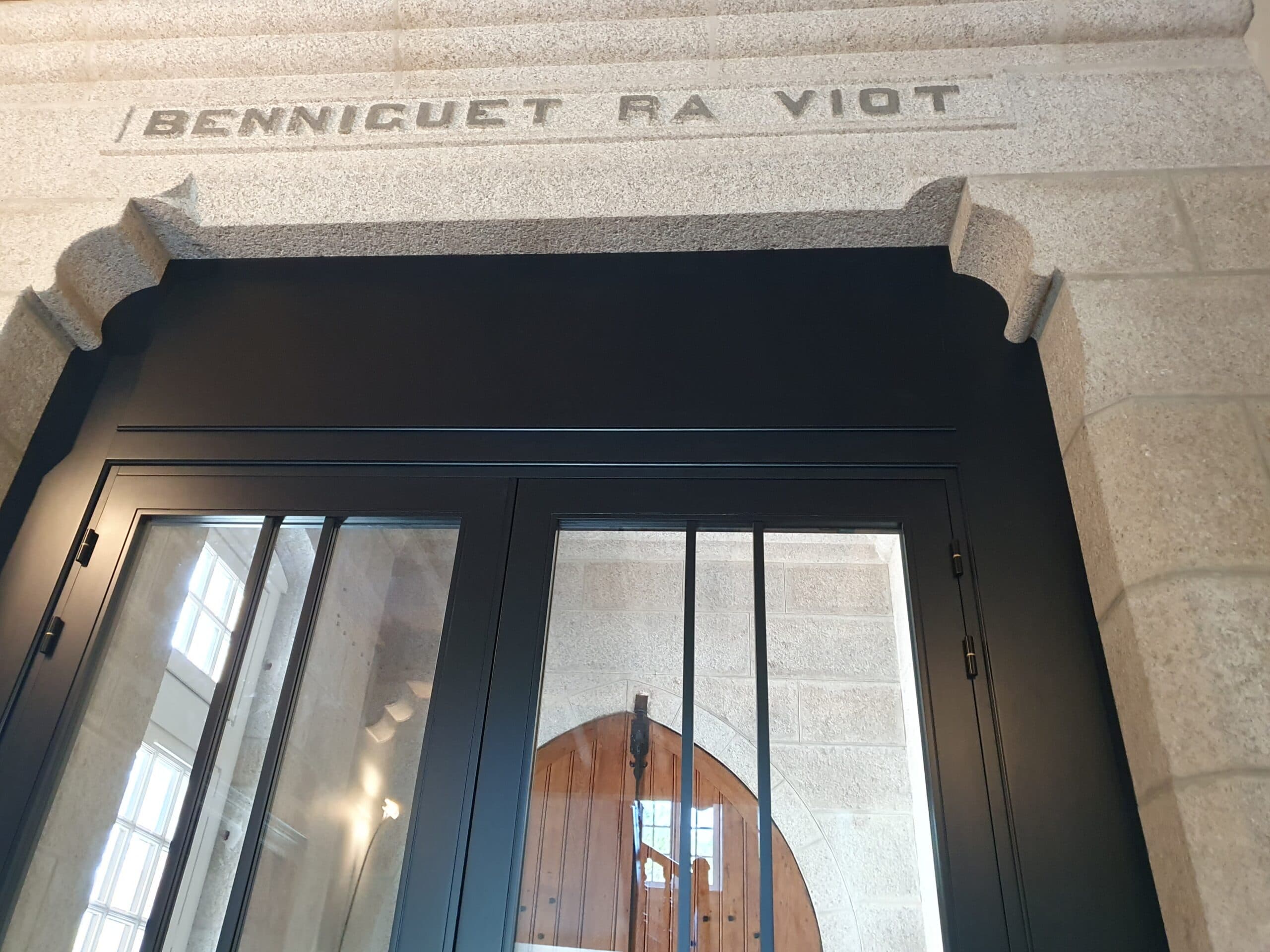 Porte d'entrée vitrée noire dans une façade en pierre