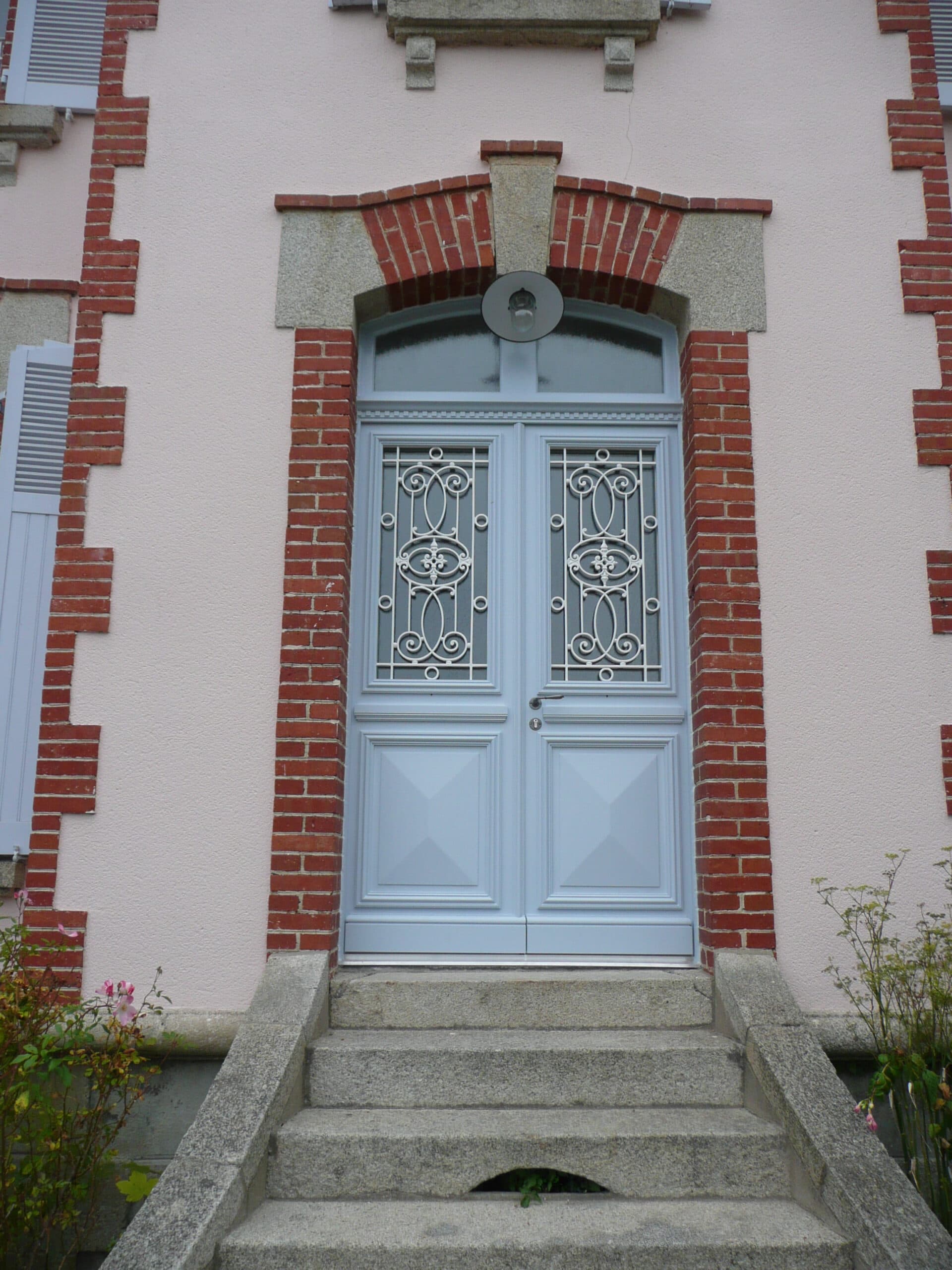 Porte d'entrée cintrée peinte en gris avec grilles en fonte