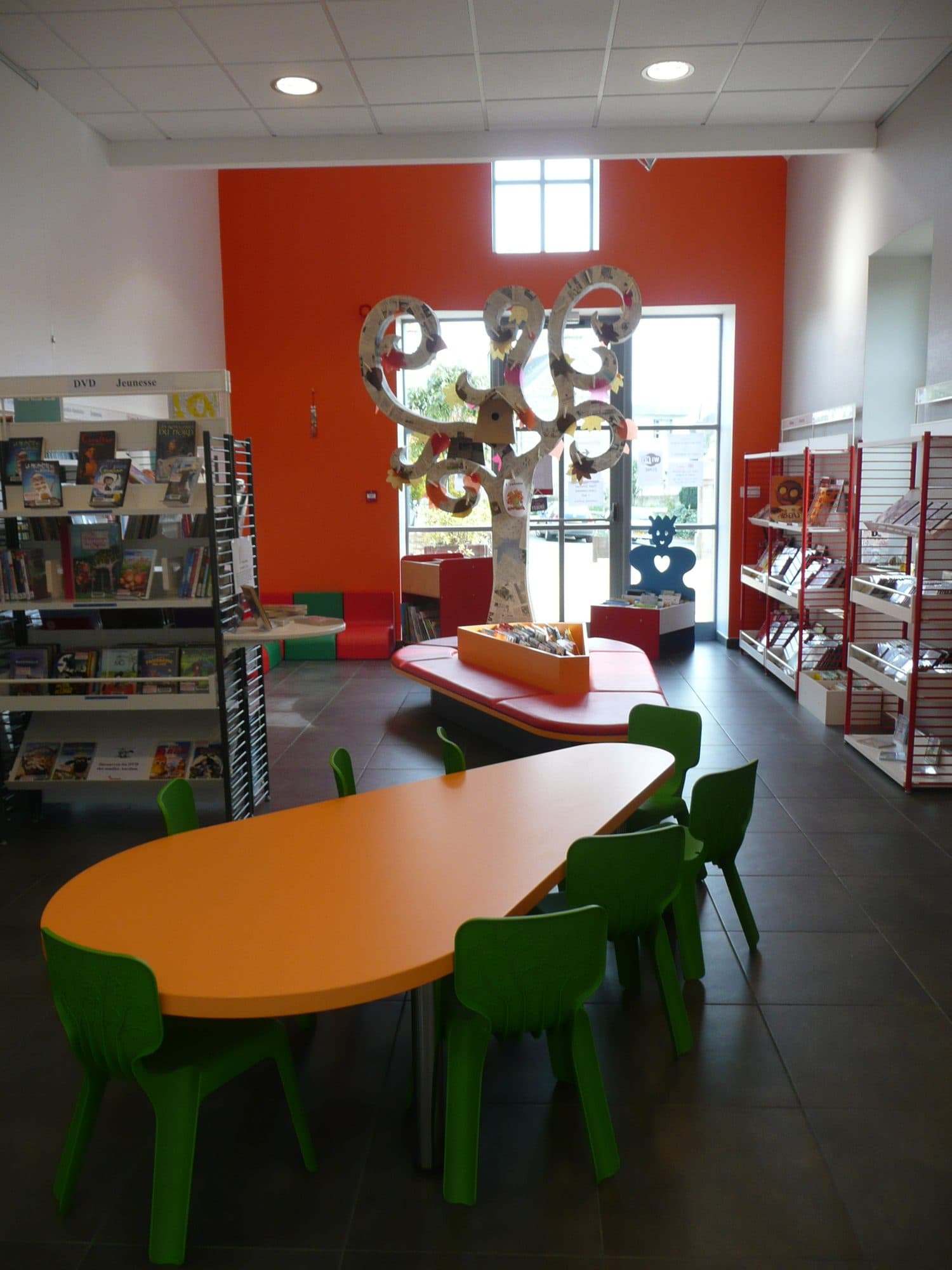 Espace jeunesse de médiathèque avec table orange et mobilier sur mesure