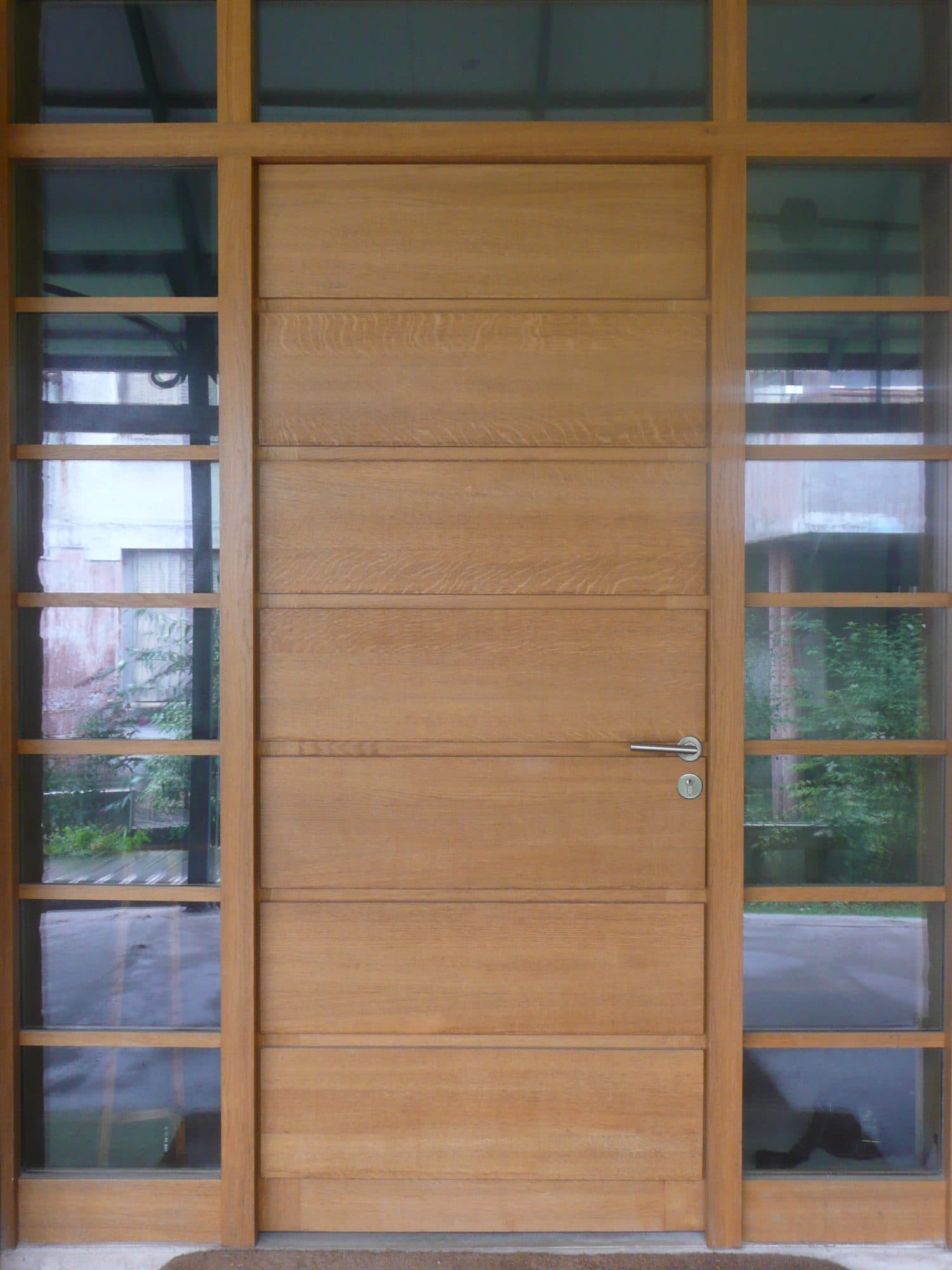 Porte d'entrée en bois à lames horizontales entourée de vitrages