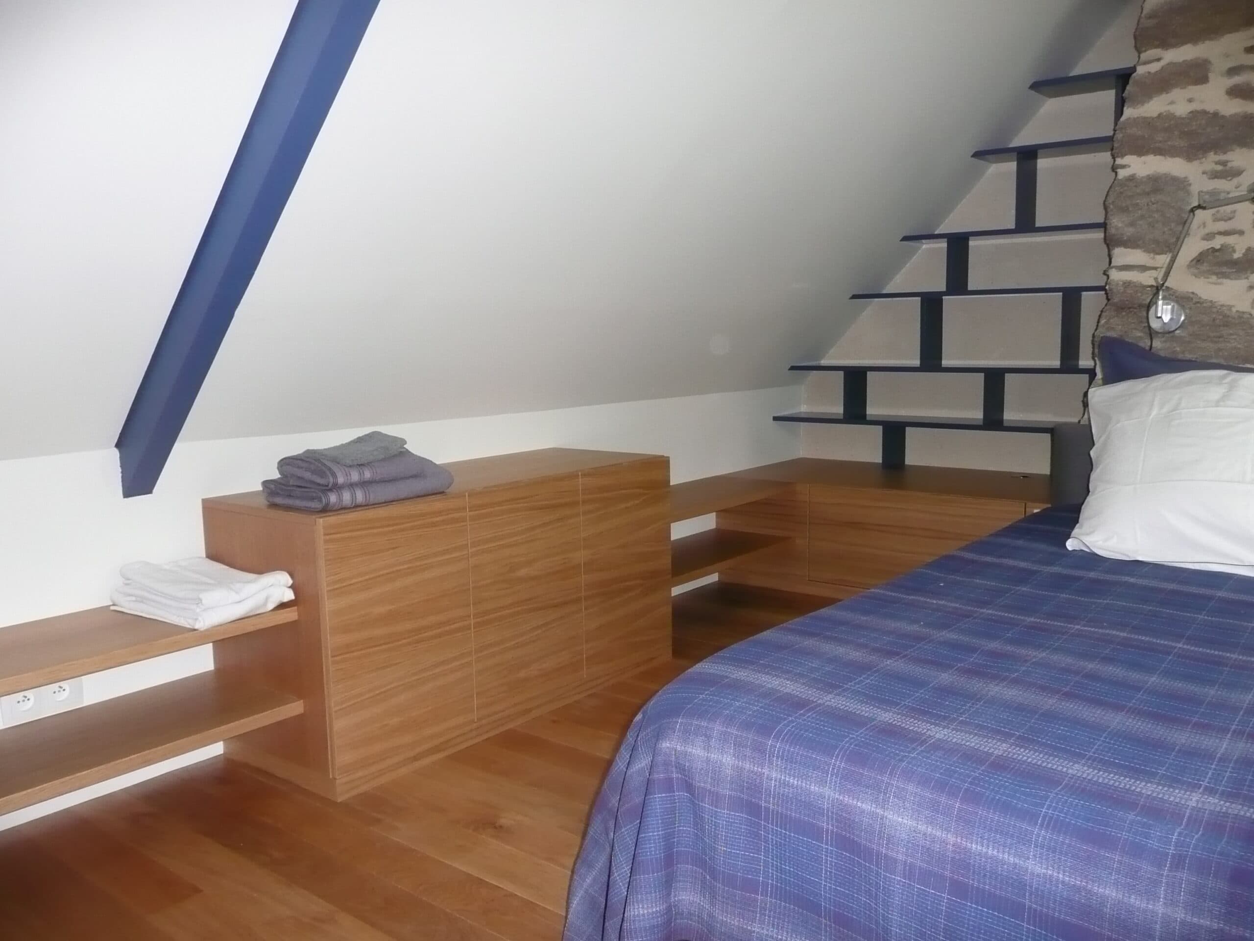 Chambre sous combles avec meuble bas en bois au pied du lit